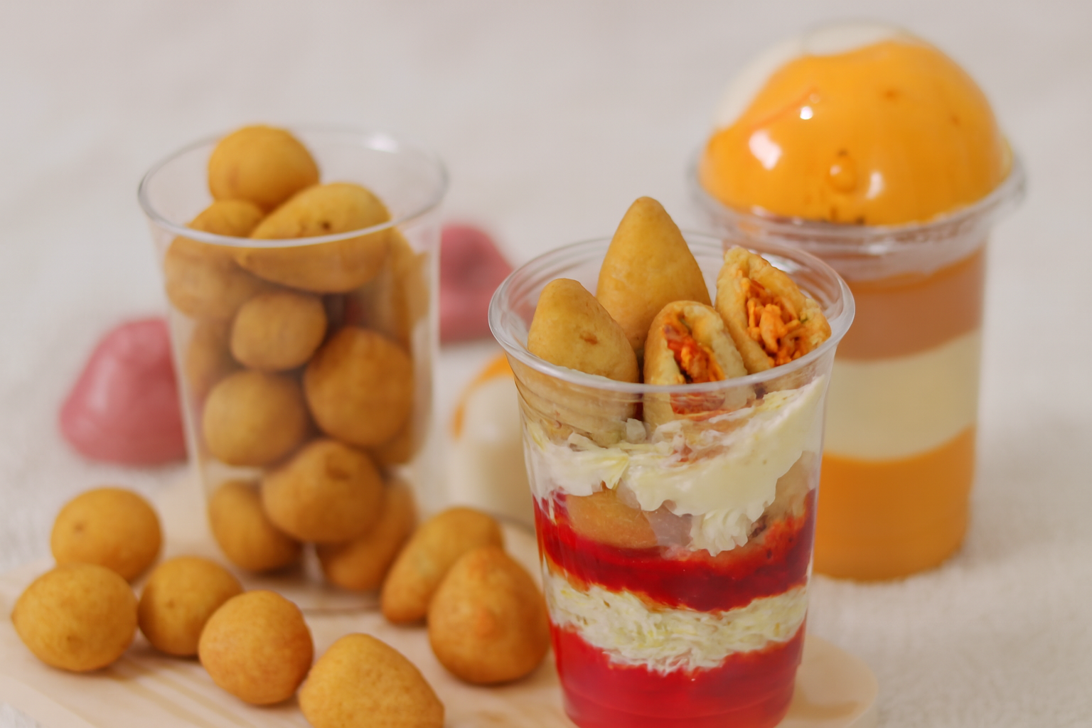 Coxinhas sobre camadas de ketchup,em copo plástico, ao lado de bolinhas de queijo