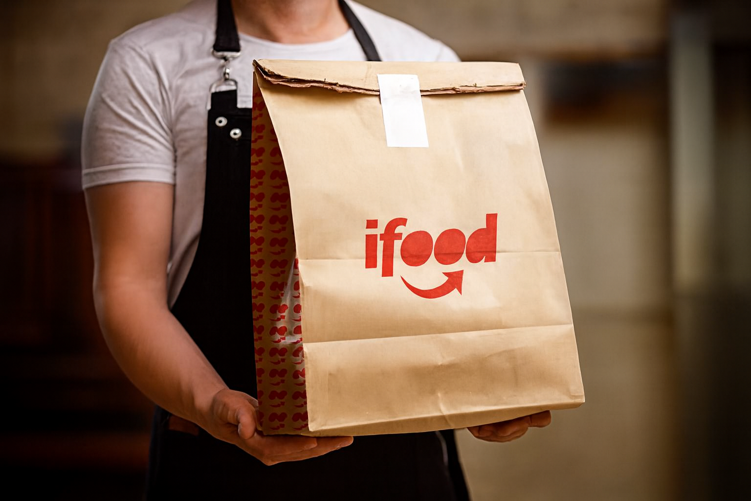 Entregador segurando sacola ifood em ambiente interno.
